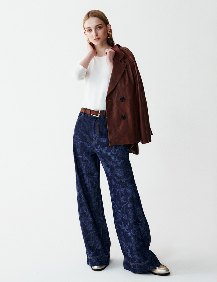 Modella indossa pantaloni di jeans in fantasia abbinati a t-shirt di colore bianco e giacca di colore marrone.